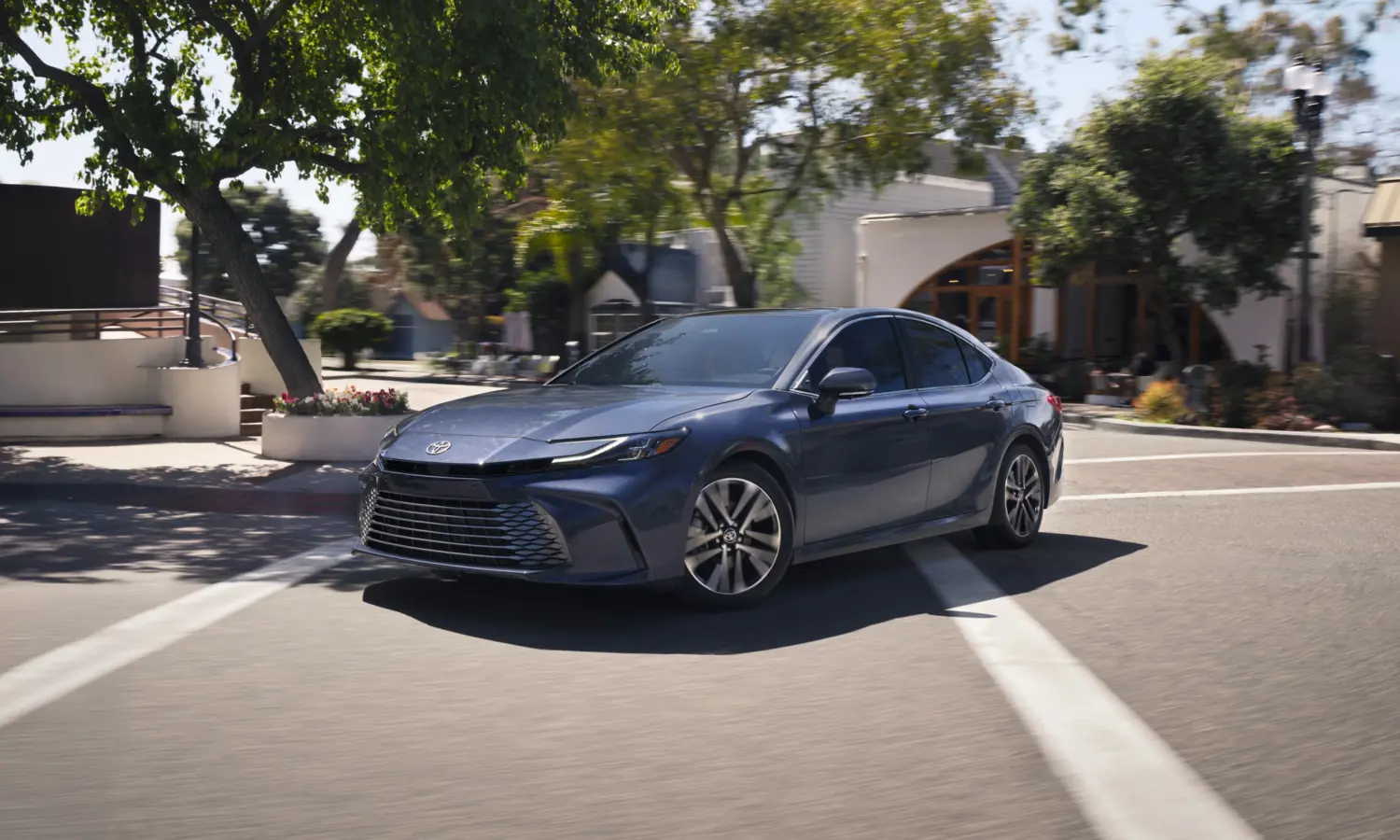 Blue Toyota Camry on a sunny street, front three-quarter view facing left