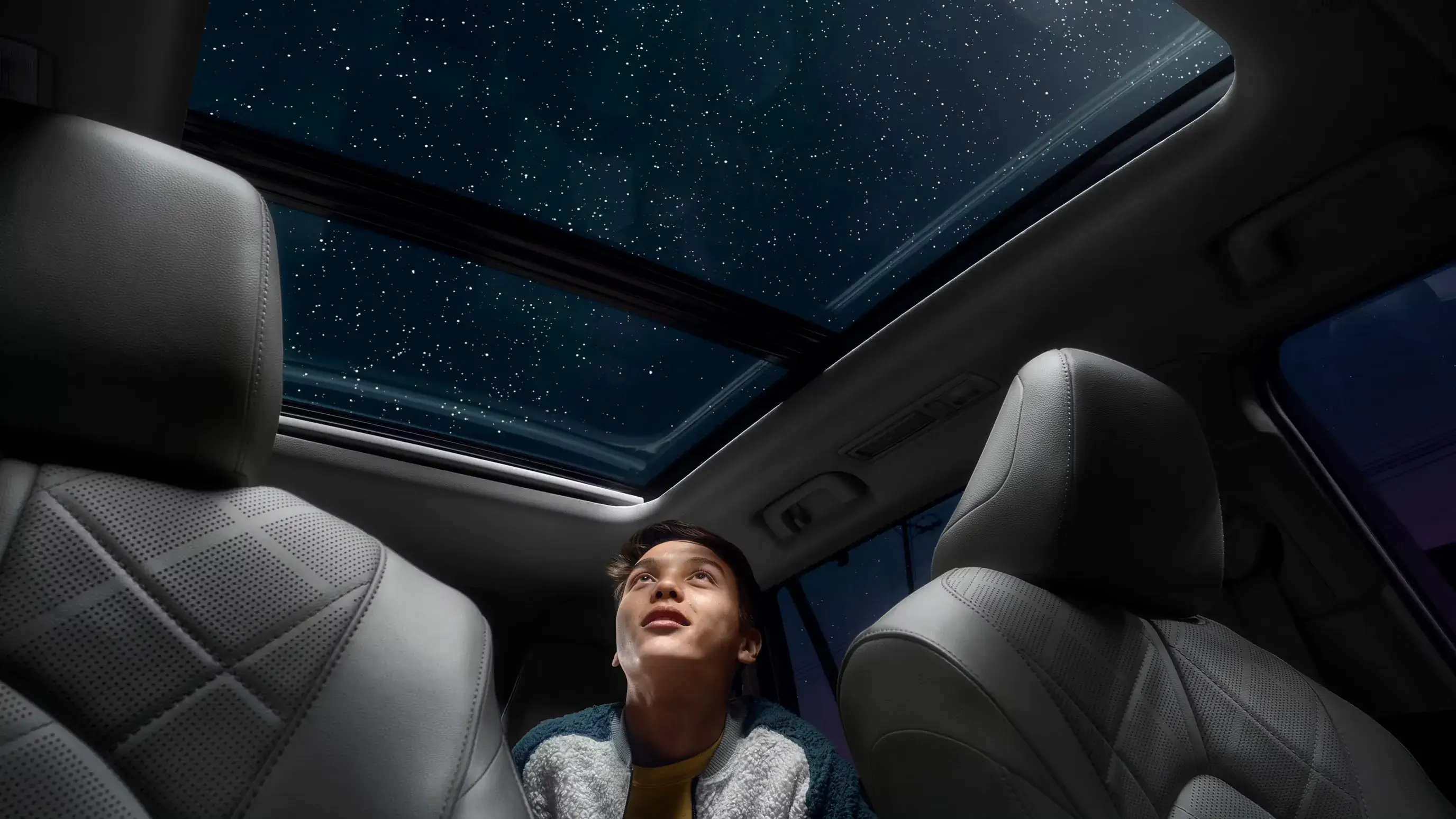 Toyota Highlander interior at night with a child looking up through the panoramic moonroof