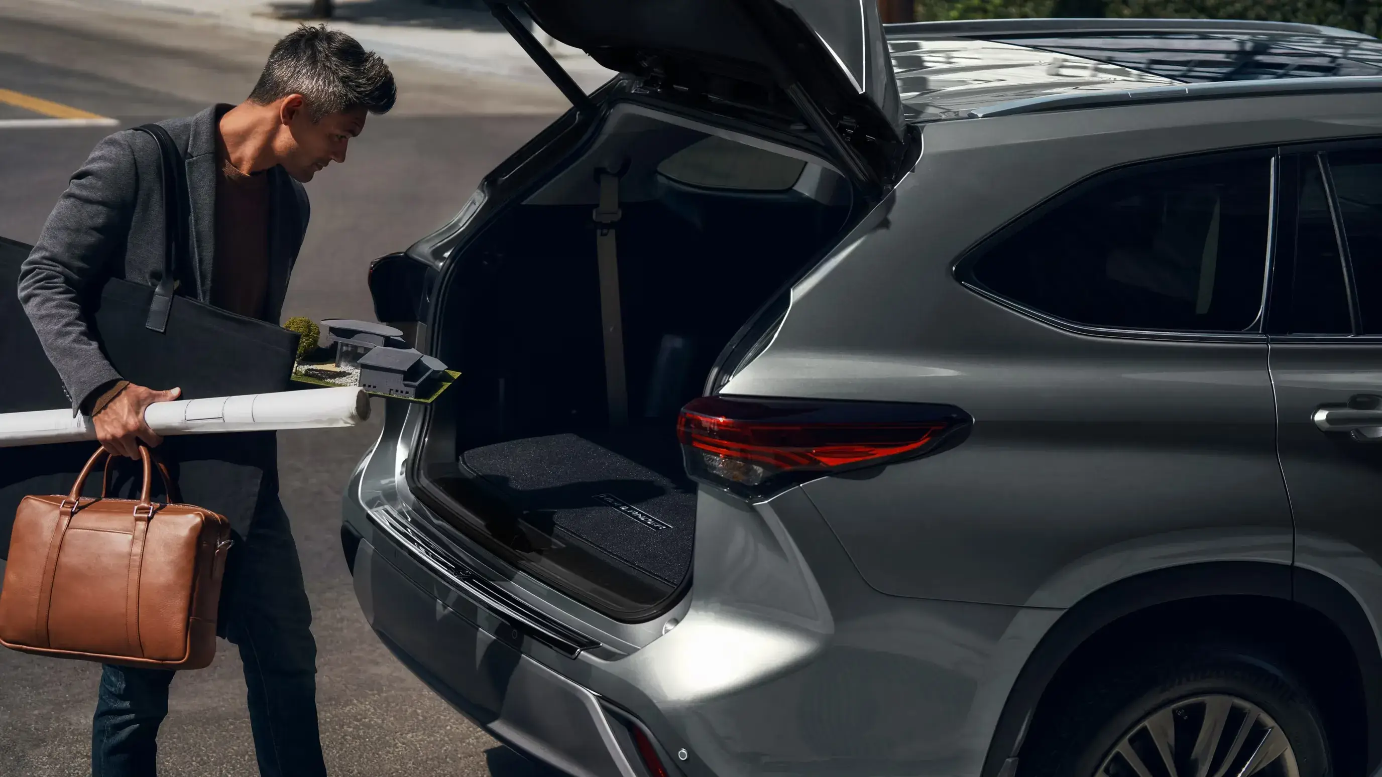 Man loading a bag into the open cargo area of a gray Toyota Highlander