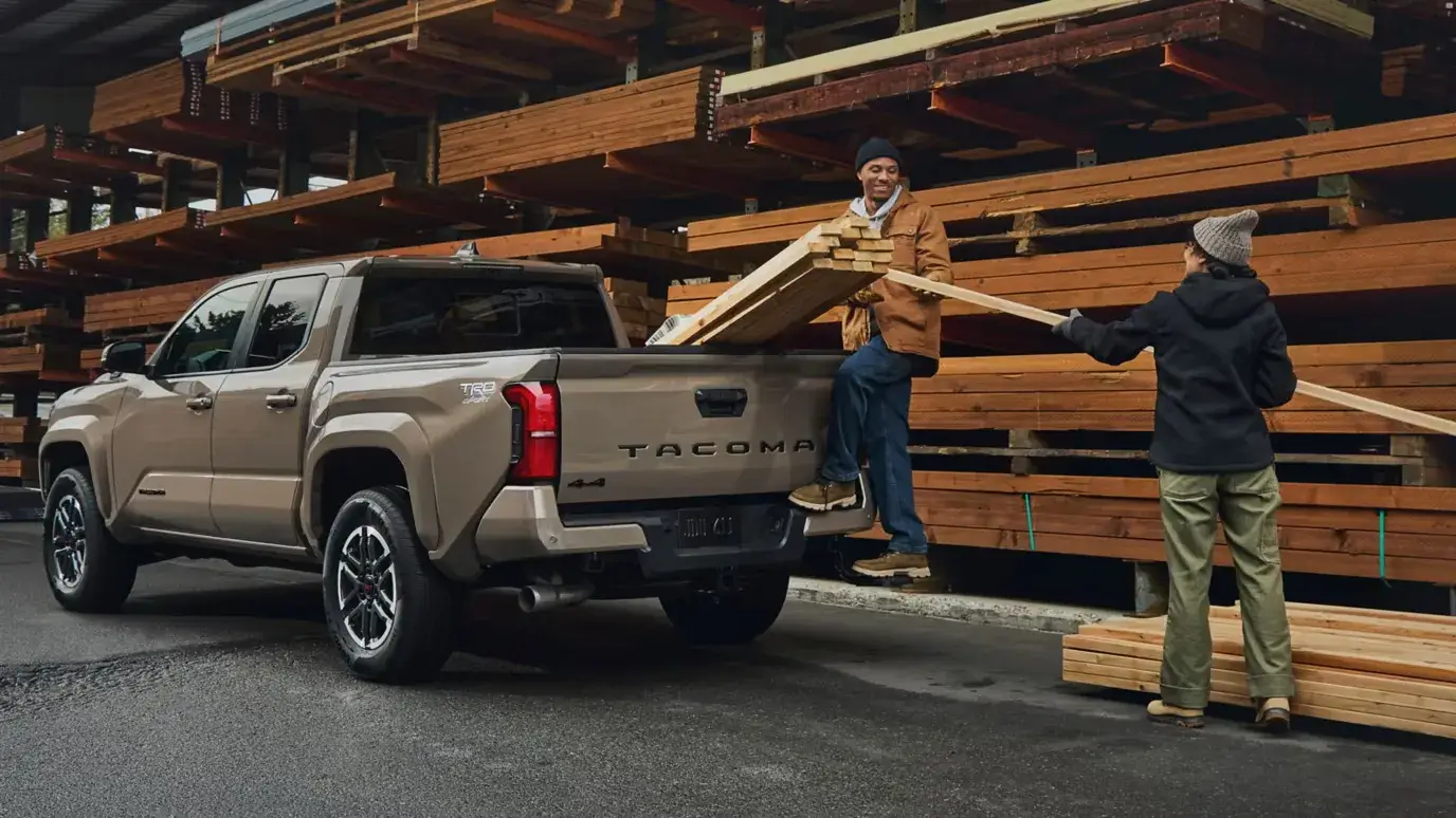 Two people loading lumber into the bed of a Toyota Tacoma i-FORCE MAX