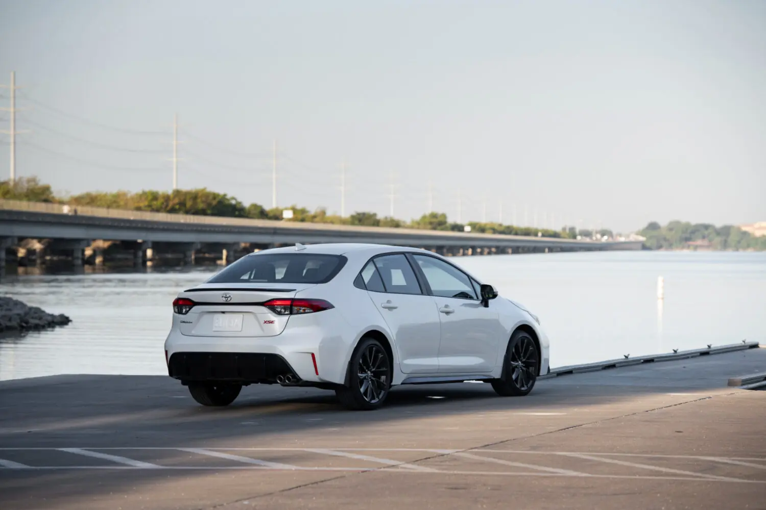 White Toyota Corolla parked by the water, rear three-quarter view from the left