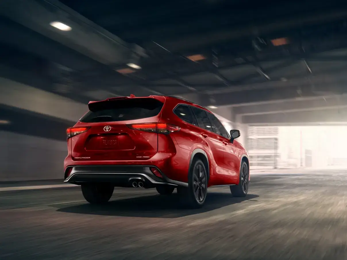 Red Toyota Highlander driving through a tunnel, rear three-quarter view from the left