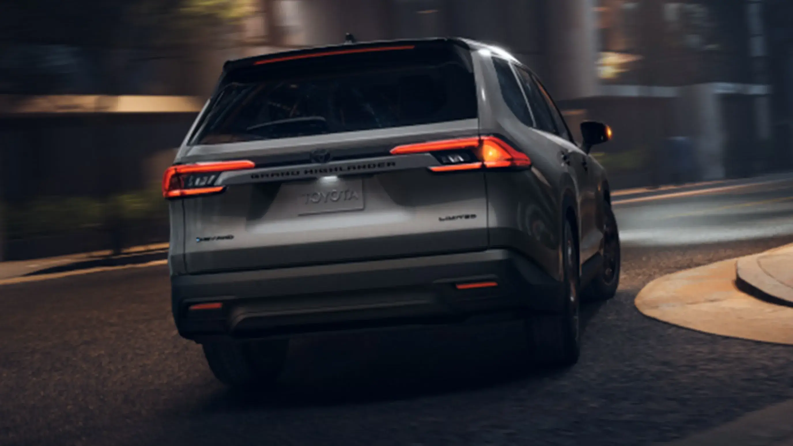 Gray Toyota Grand Highlander driving at night, rear three-quarter view from the left