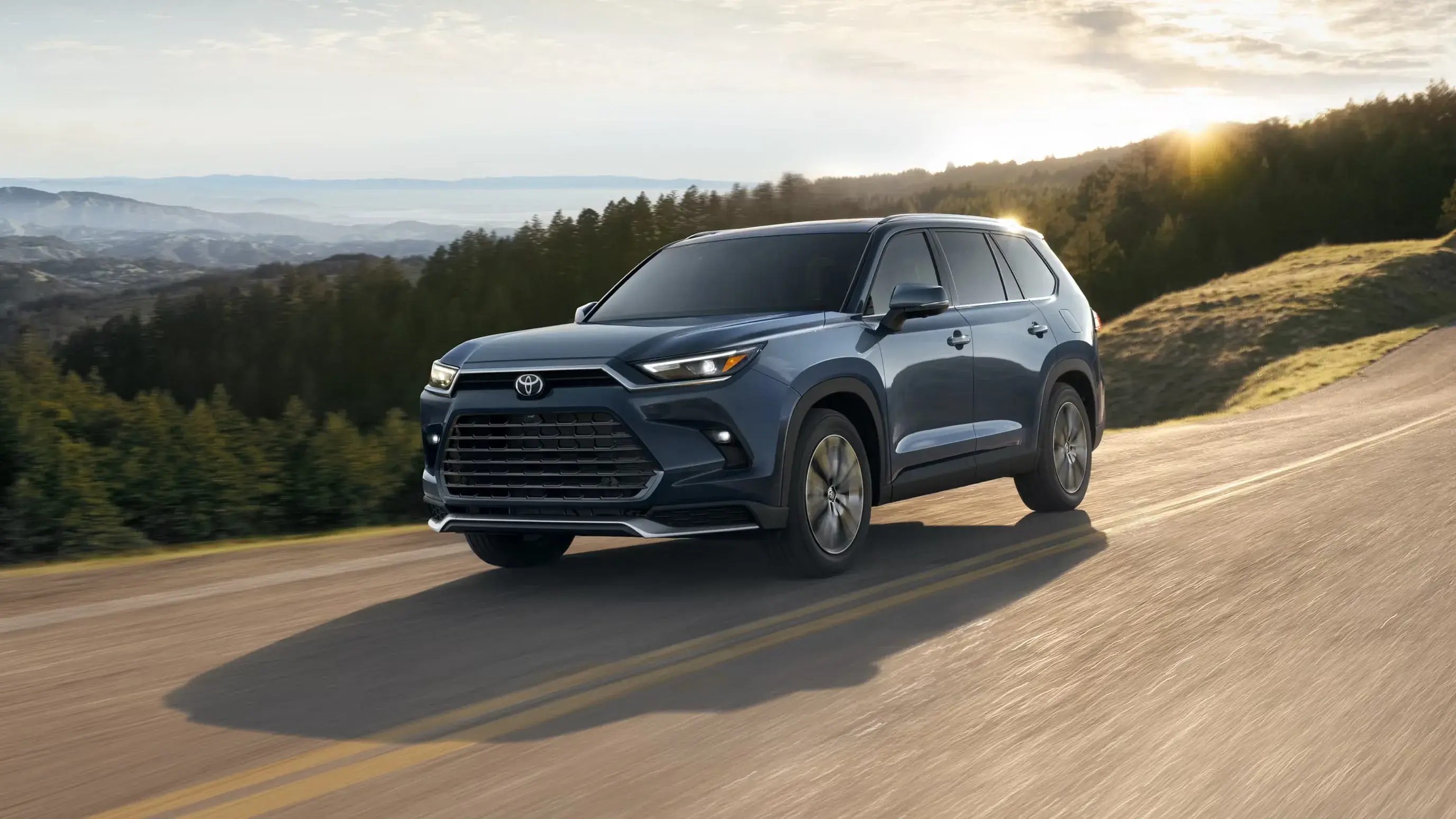 Blue Toyota Grand Highlander driving on a hillside road, front three-quarter view facing left