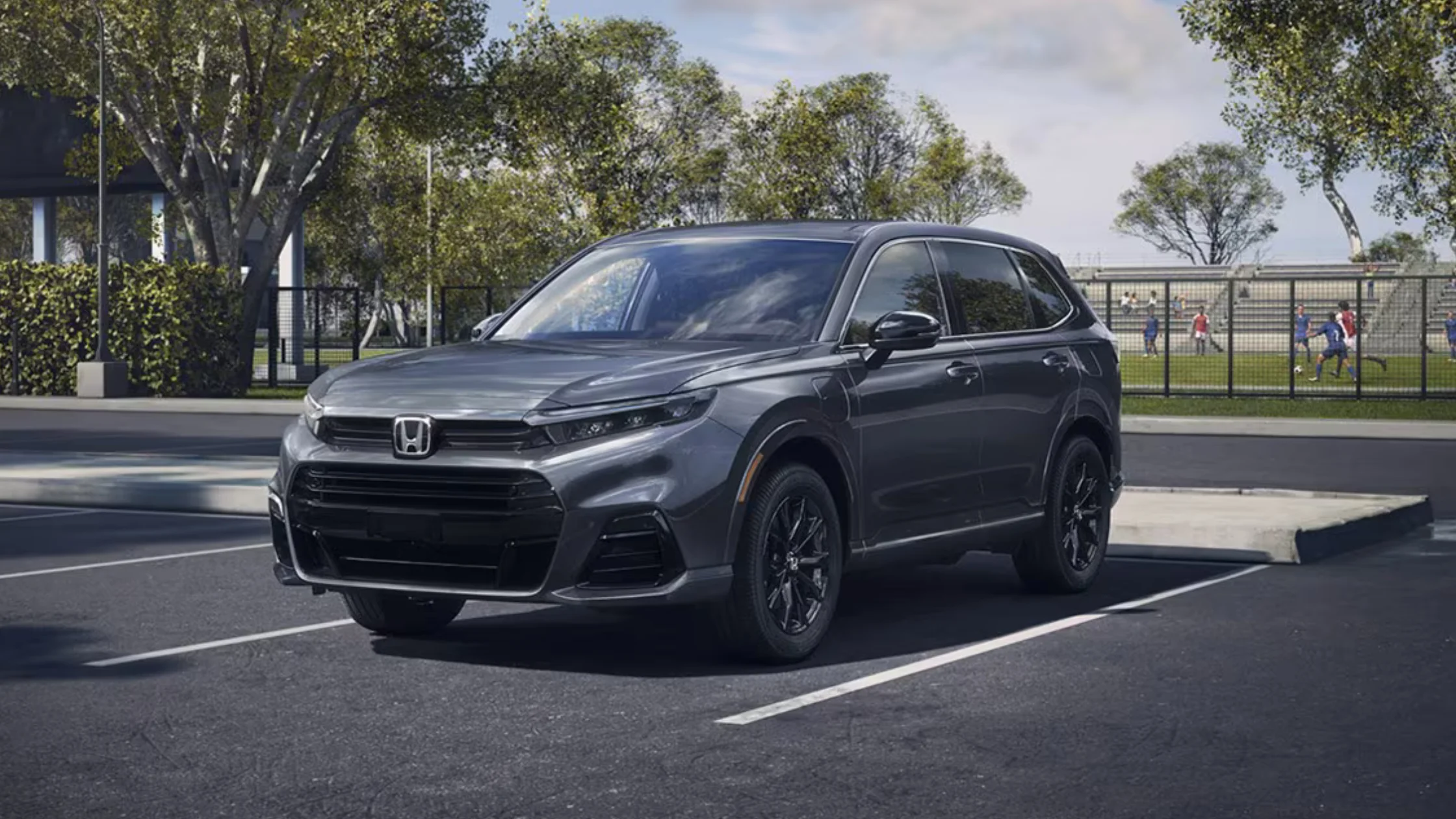 2026 Honda CR-V e:FCEV electric SUV in gray parked near soccer field, highlighting front fascia and charging port.