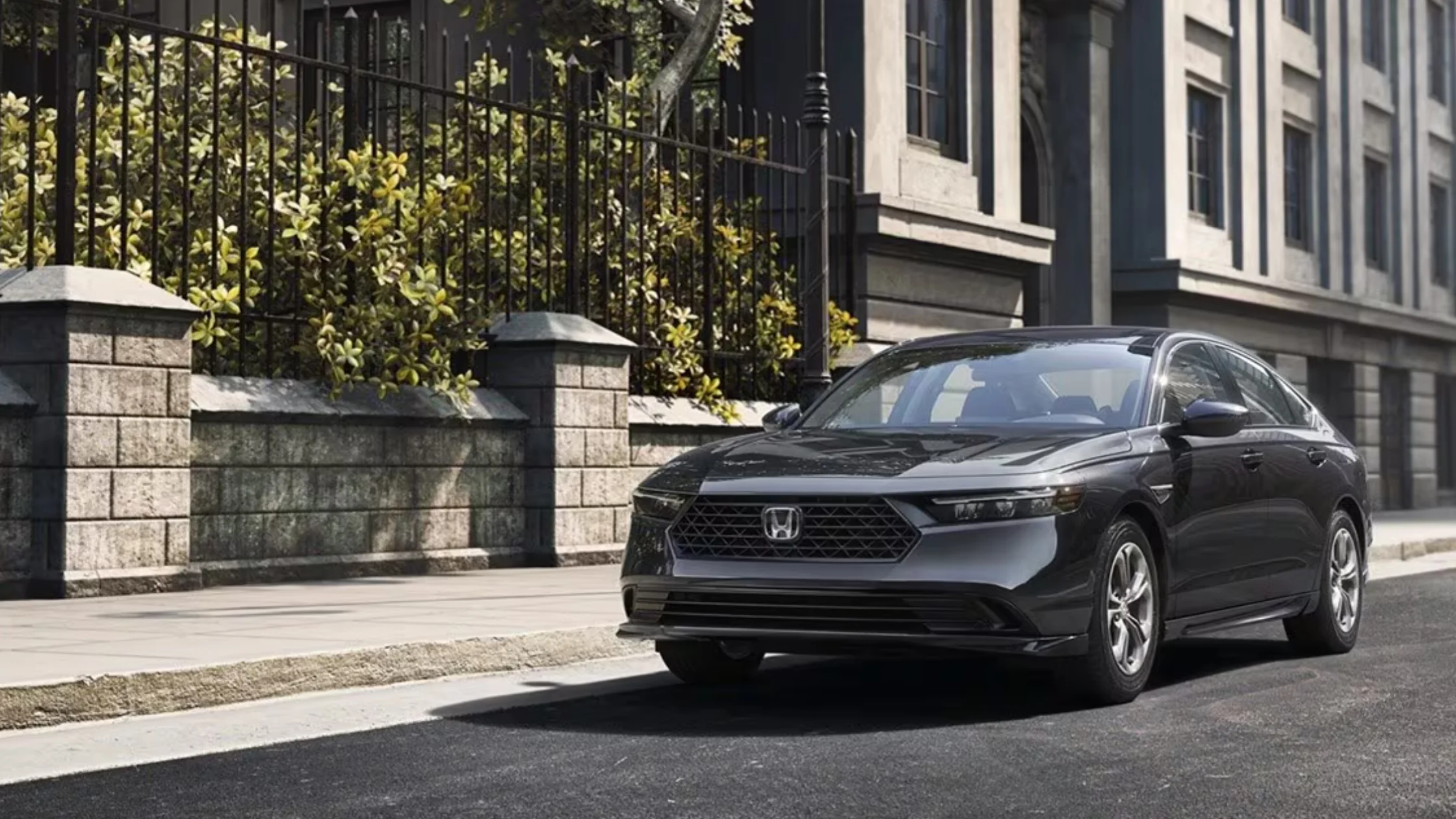 2026 Honda Accord Hybrid parked on urban street in gray, showing sleek front grille and aerodynamic body lines.