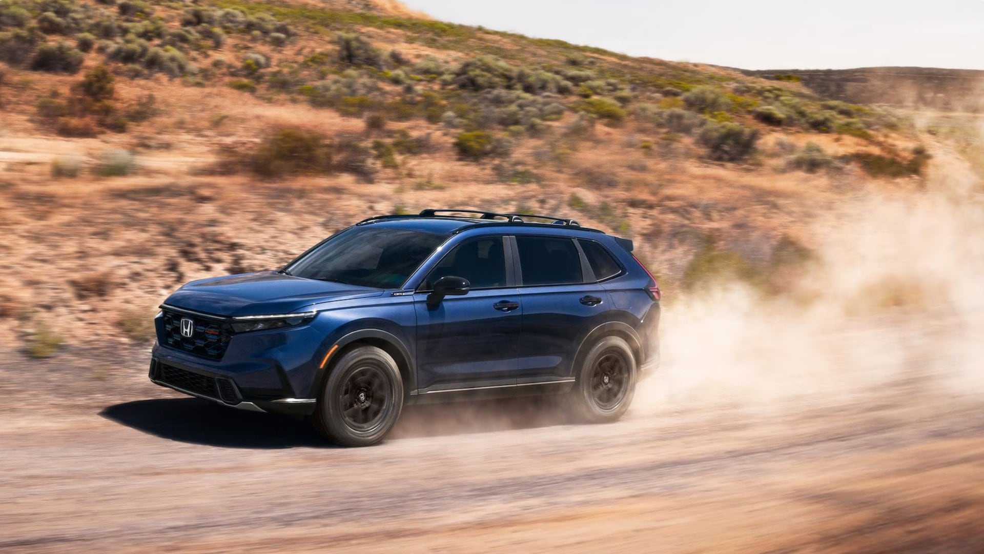 Blue 2026 Honda CR-V Hybrid driving on a dusty dirt road with off road scenery