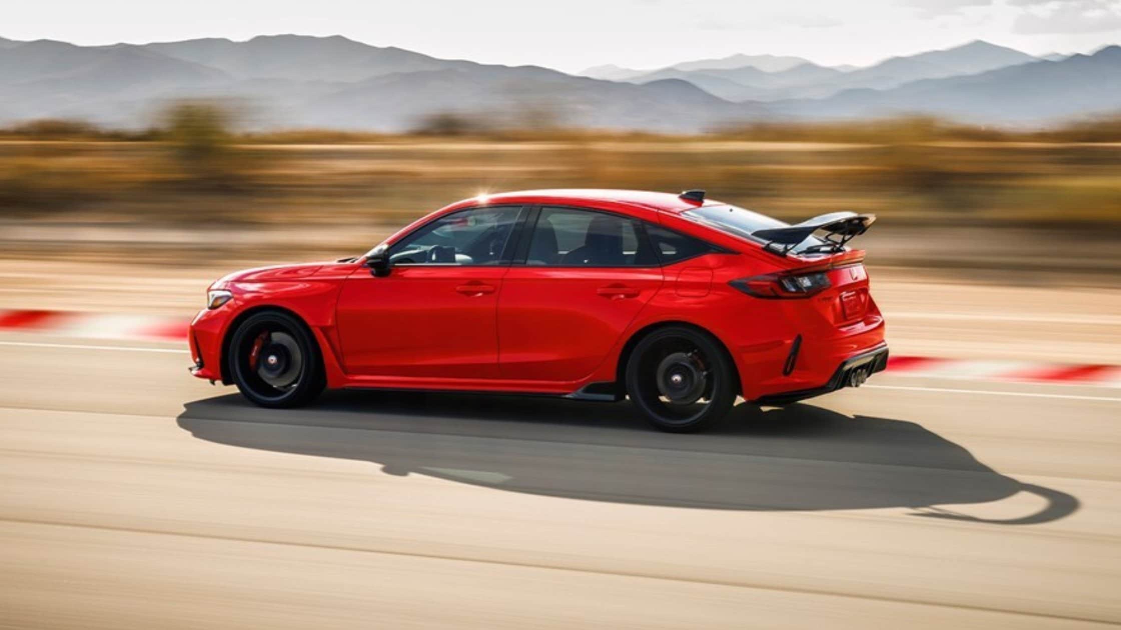 2025 Honda Civic Type R in red speeding on a race track with rear wing and black performance wheels.