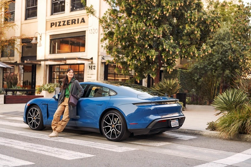 Woman leaning up against blue Porsche Taycan