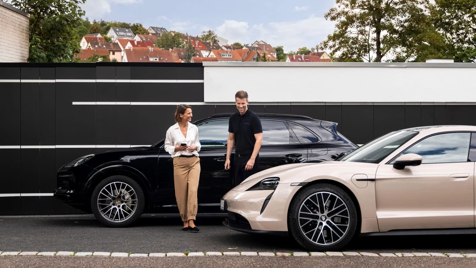A happy Porsche Drive customer walking from a Porsche Cayenne to a Porsche Taycan