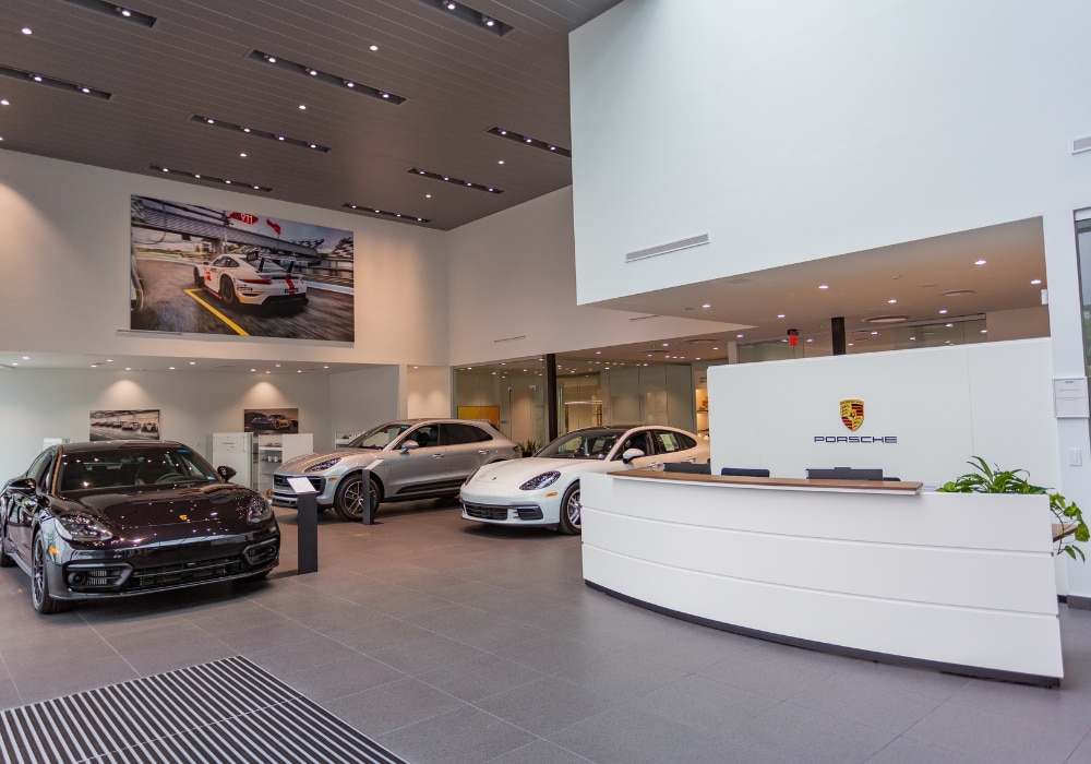 Three Porsche cars for sale parked inside the showroom of the Porsche Charlottesville. The front desk of the dealership is also visible in the photo