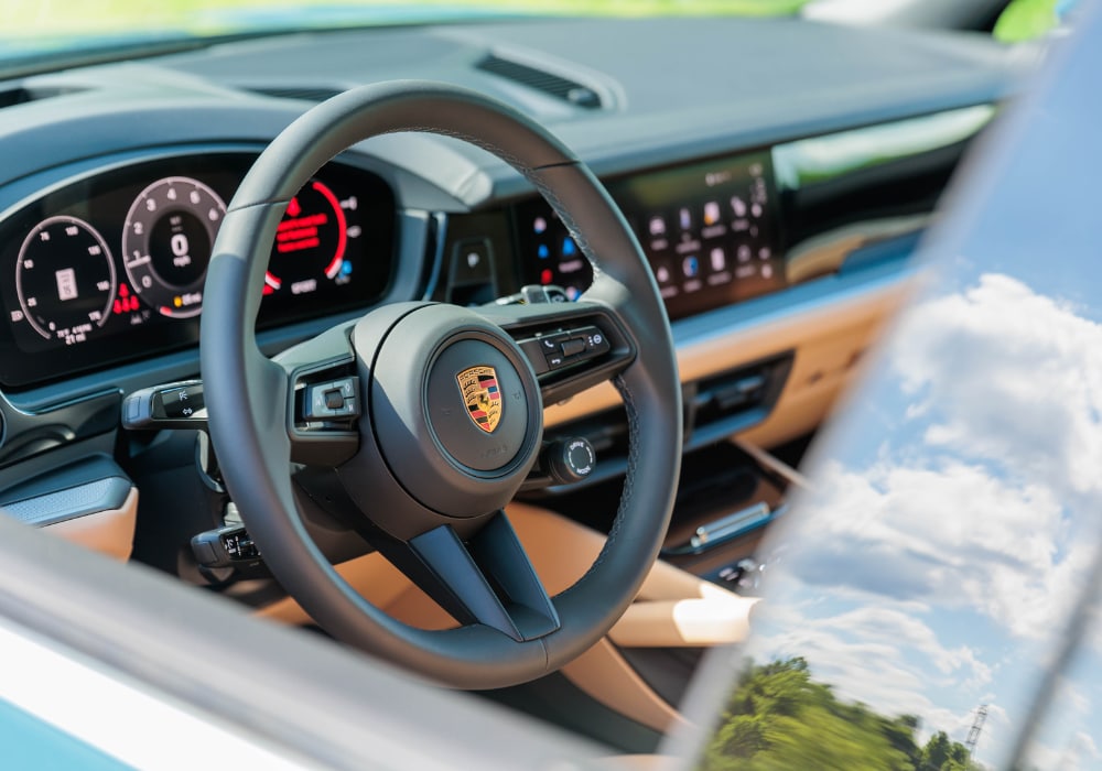 Close up photo of the interior of the 2025 Porsche Cayenne, specially the front dash. The Porsche logo is visible on the steering wheel of the car