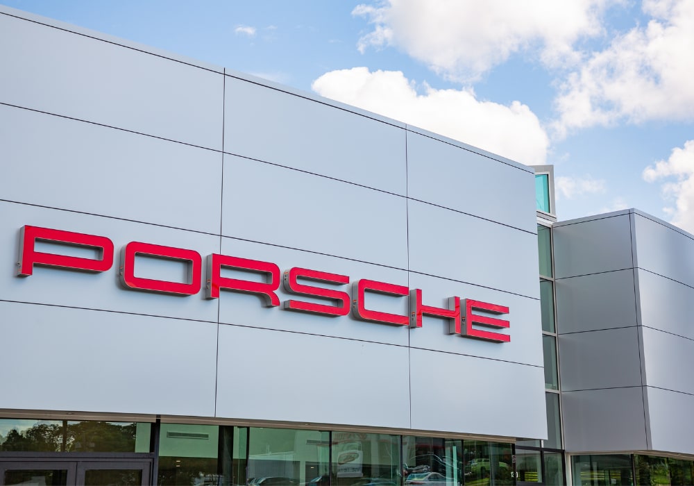 Exterior storefront of a Porsche dealership in Charlottesville. The Porsche logo is attached to the front of the dealership in red lettering