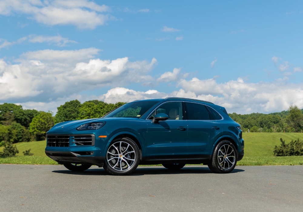 Blue Porsche Cayenne for sale parked in front of a big field. There is a blue sky in the background