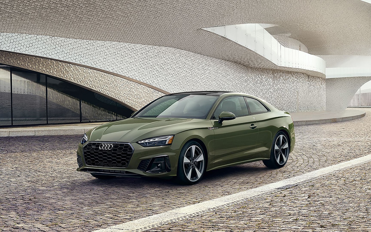 green Audi parked in the entryway of a white tiled modern building