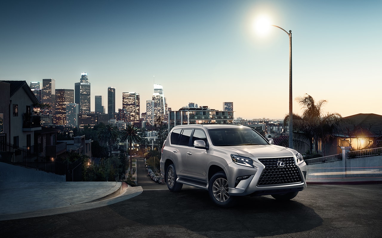 silver Lexus SUV at the top of a road's hill, overlooking a city