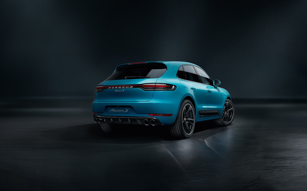 teal Porsche Macan parked in a black room