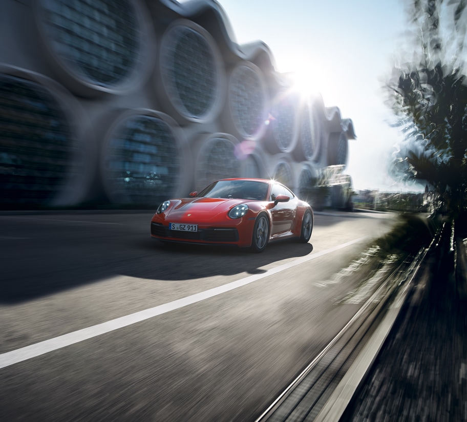 red Porsche 911 Carrera Coupe driving past a modern glass building