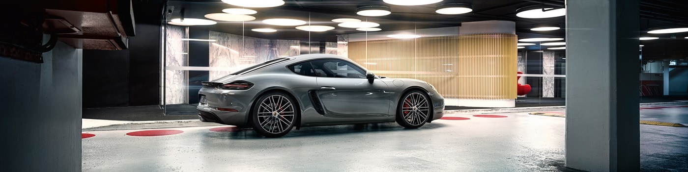 Grey Porsche 718 Cayman parked beside a modern building in a parking garage