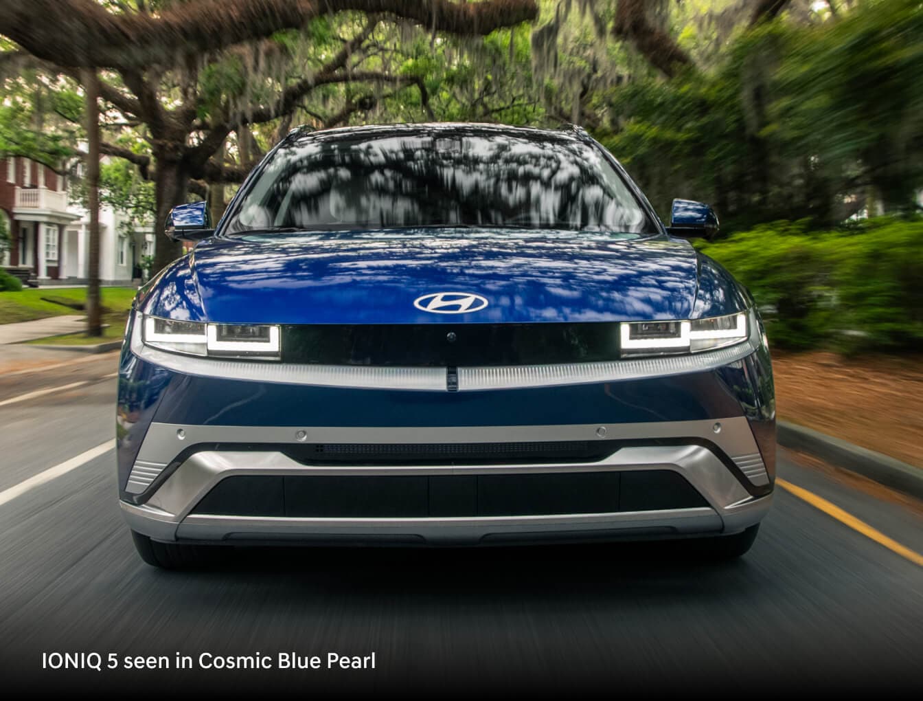 2026 Hyundai IONIQ 5 in Cosmic Blue Pearl, front view driving along a tree-lined residential street.