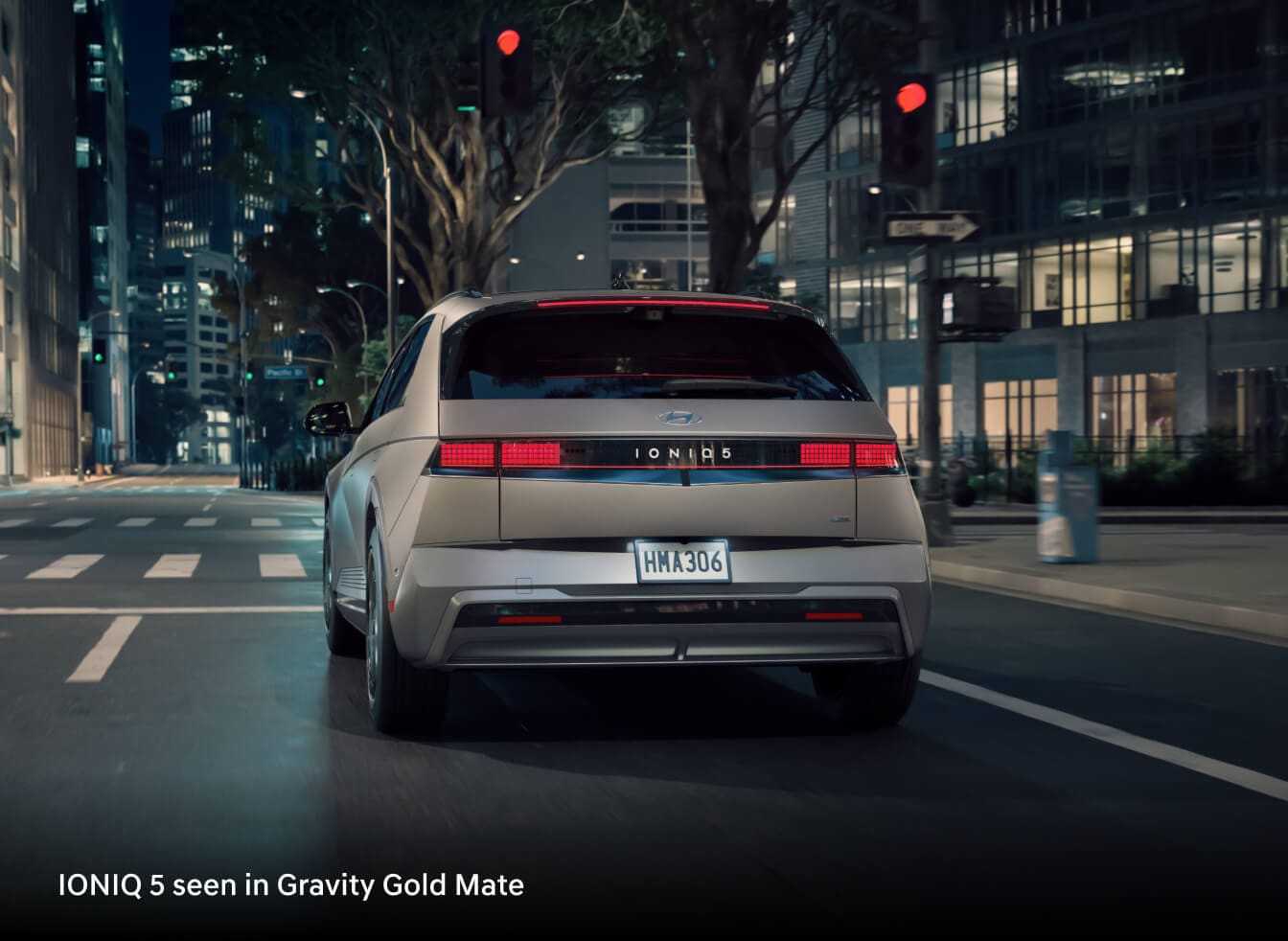 2026 Hyundai IONIQ 5 Limited in Gravity Gold Matte, rear view driving through a city street at night.