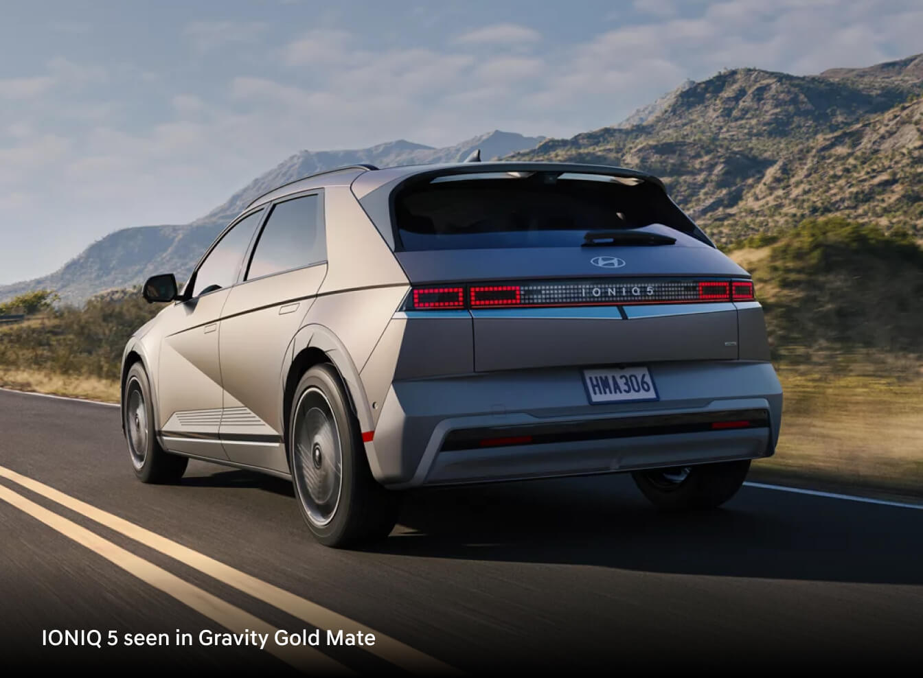 2026 Hyundai IONIQ 5 in Gravity Gold Matte, rear three-quarter view driving on mountain road.
