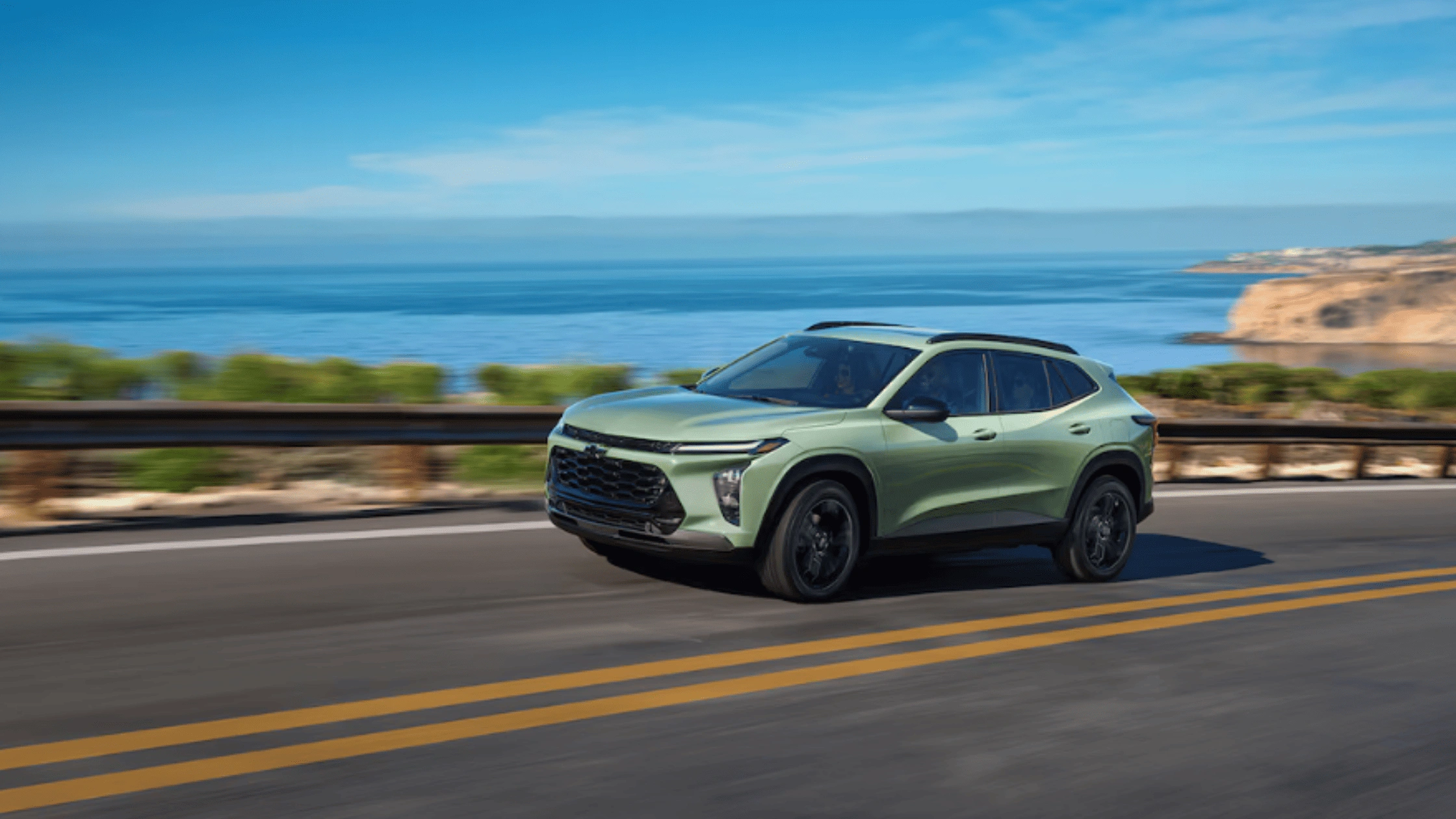 2026 Chevrolet Trax in green driving along a coastal highway, highlighting compact SUV style and efficiency near Fort Bragg, NC.