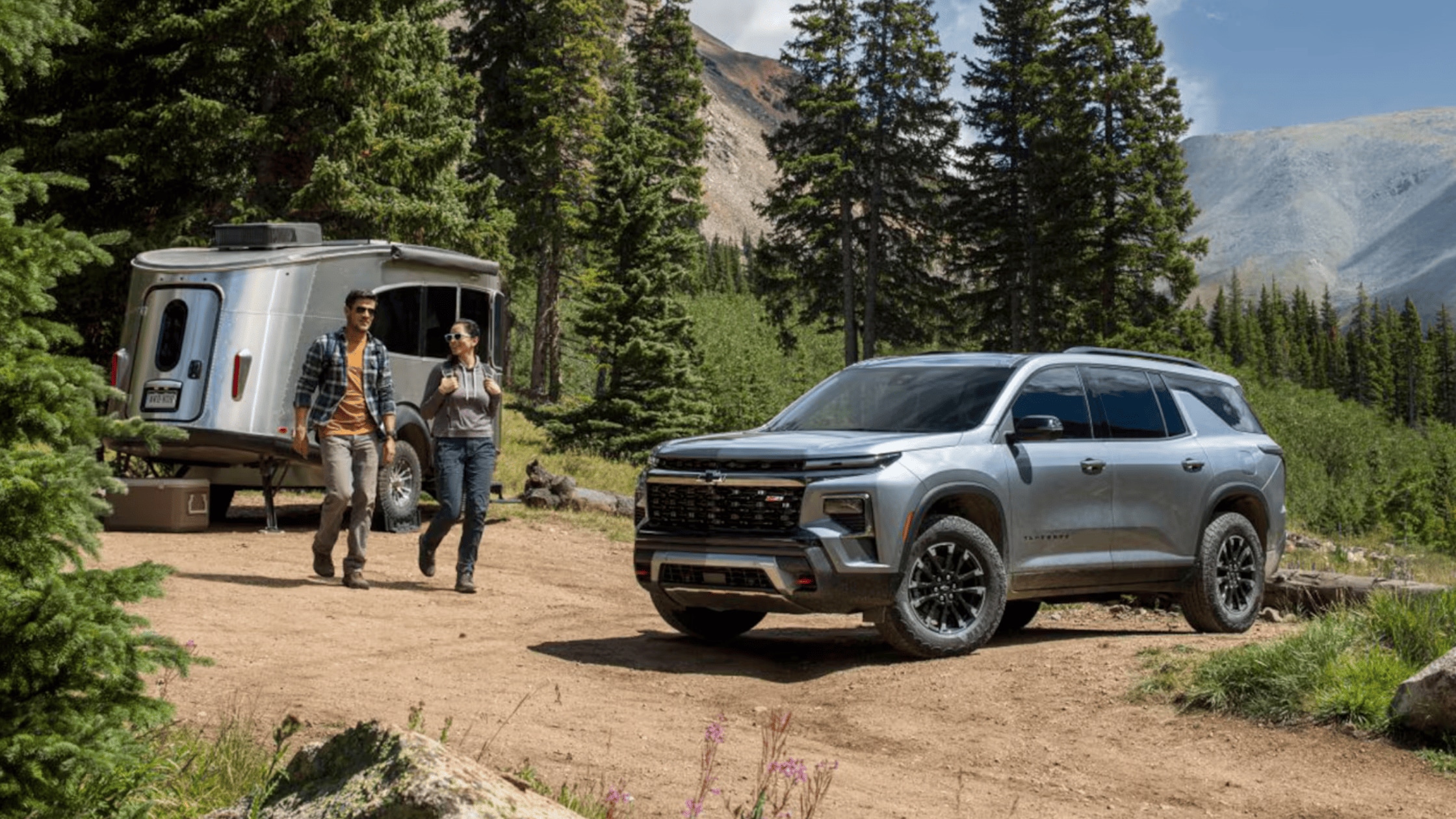 2025 Chevrolet Traverse in silver parked at a campsite with a trailer, balancing tech, comfort, and space for Fayetteville adventures.