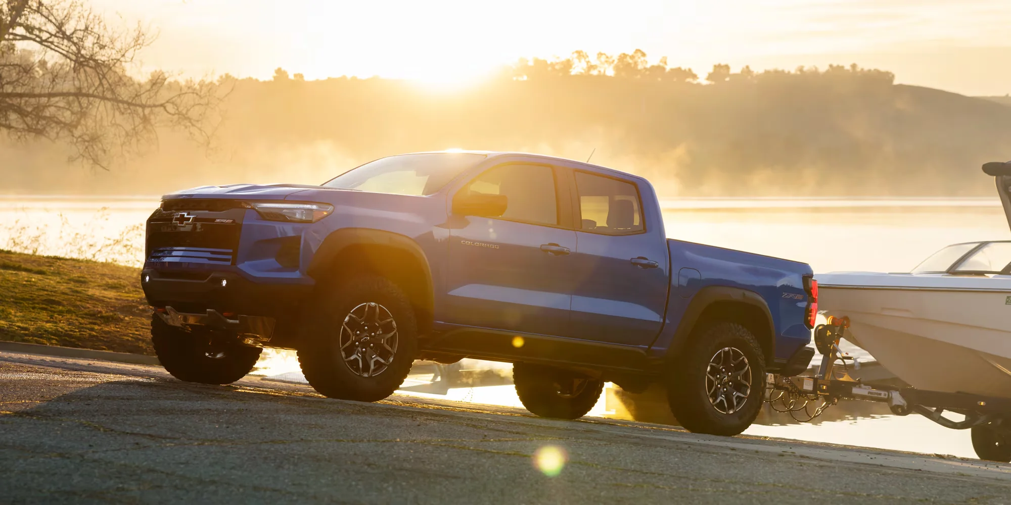 2026 Chevy Colorado towing a boat at sunrise near a lake