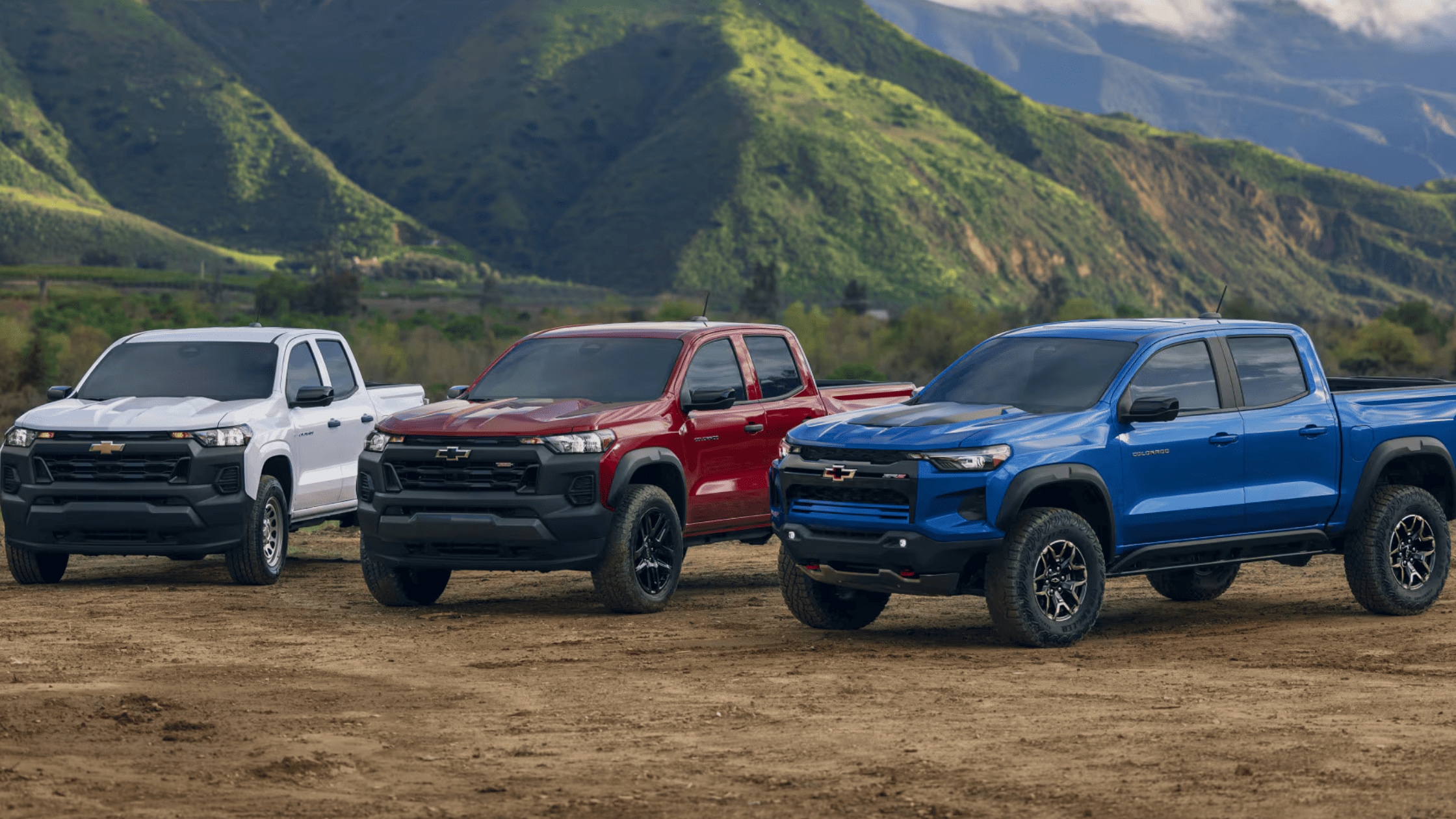 2025 Chevrolet Colorado in white, red, and blue parked on a dirt road with scenic mountains in the background, ideal for rough terrain in Fayetteville