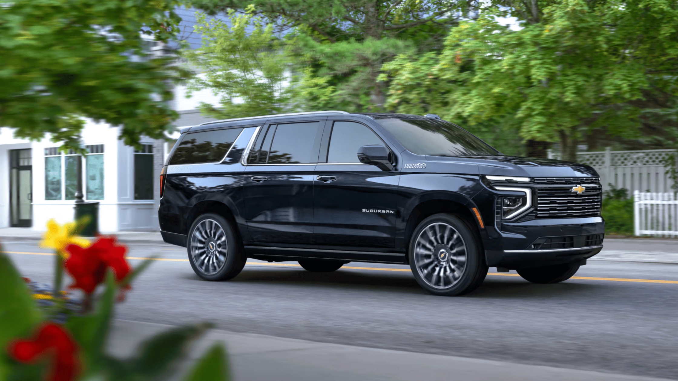 2025 Chevrolet Suburban in black driving through a suburban street, showcasing its spacious interior and comfort for family road trips in Fayetteville.