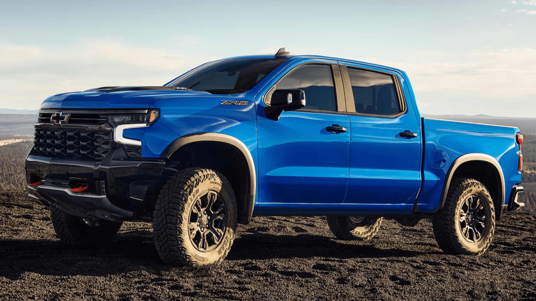 2025 Chevrolet Silverado in blue parked on rugged terrain under clear skies, showcasing its powerful engine and versatile trims for Fayetteville drivers.