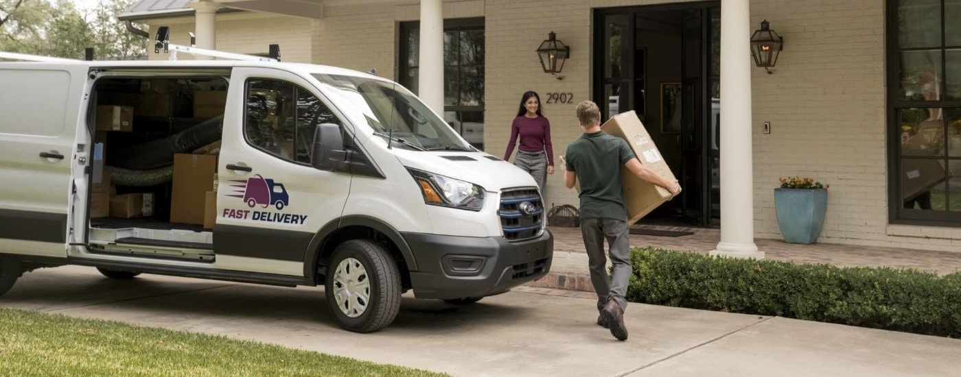 A delivery man carries a package out of a white 2023 Ford E-Transit.