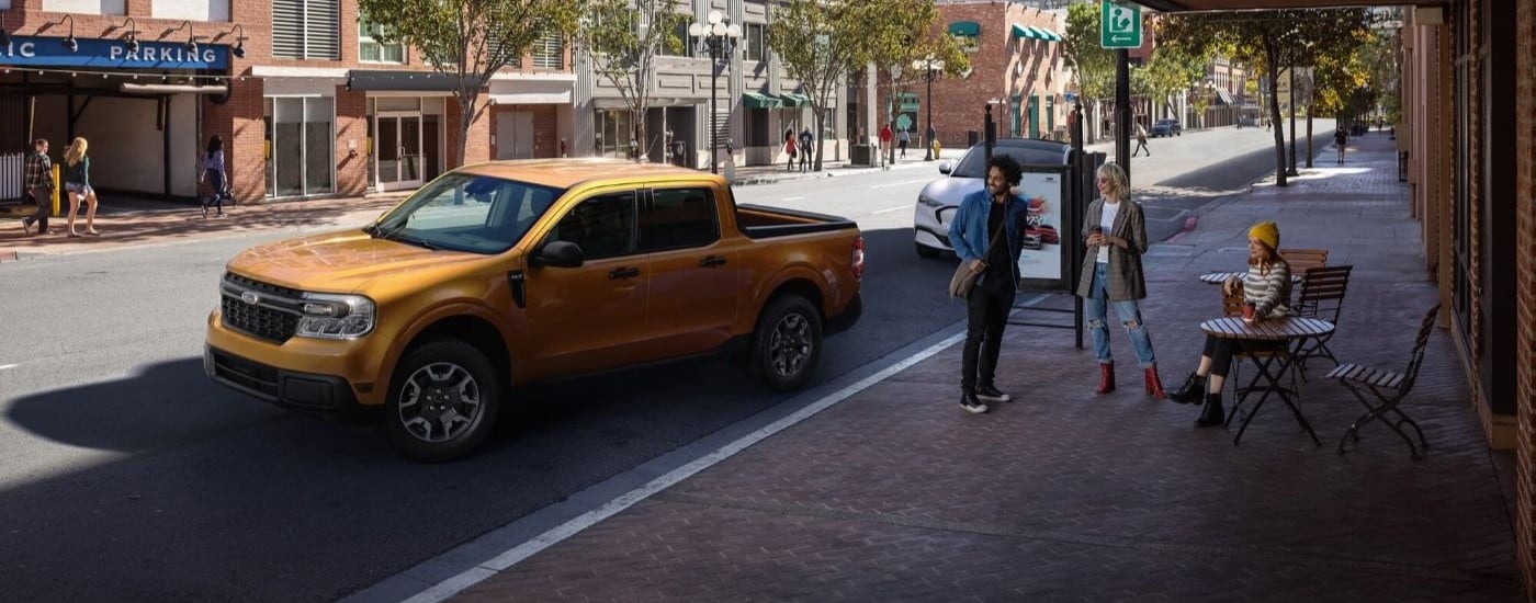 A yellow 2023 Ford Maverick parked on a city street near a cafe after leaving a Ford dealer near Queens.