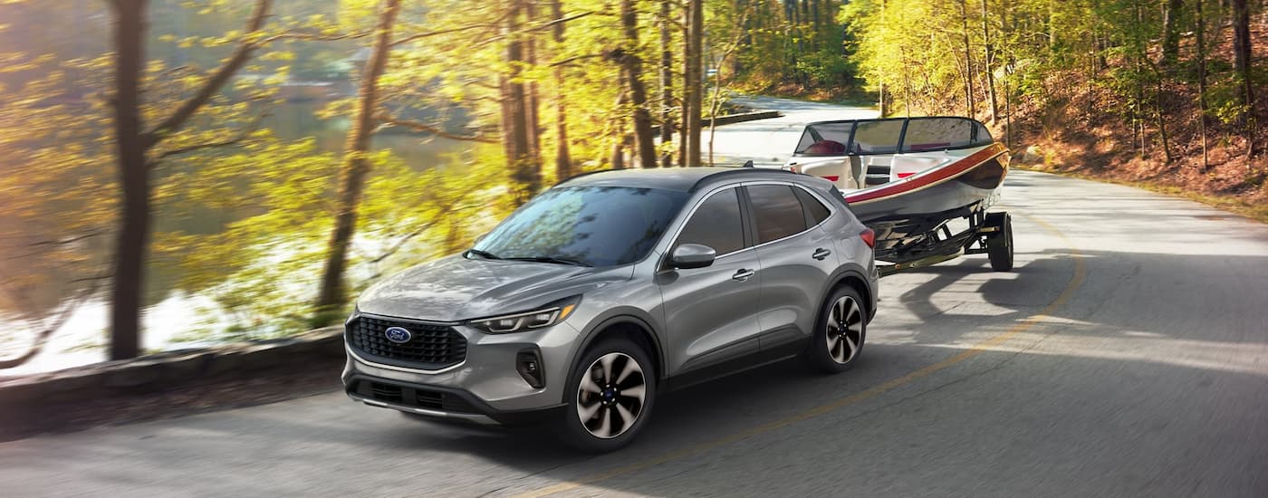 A silver 2024 Ford Escape is shown towing a boat on a winding road.
