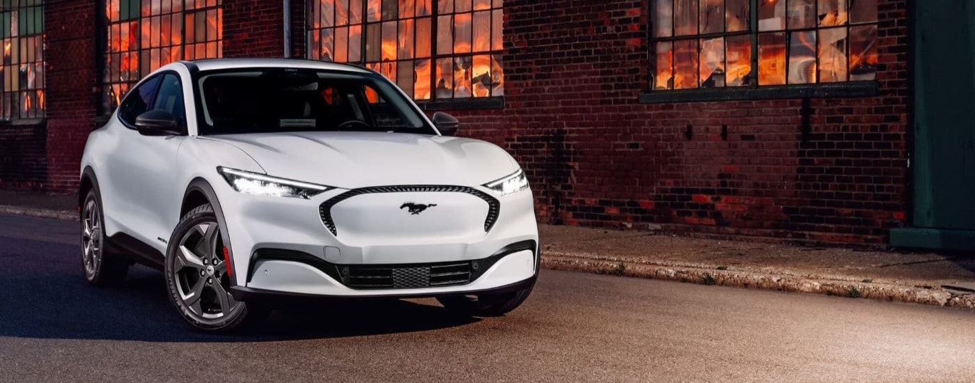 A white 2023 Ford Mustang Mach-E parked near a brick building with glowing windows.