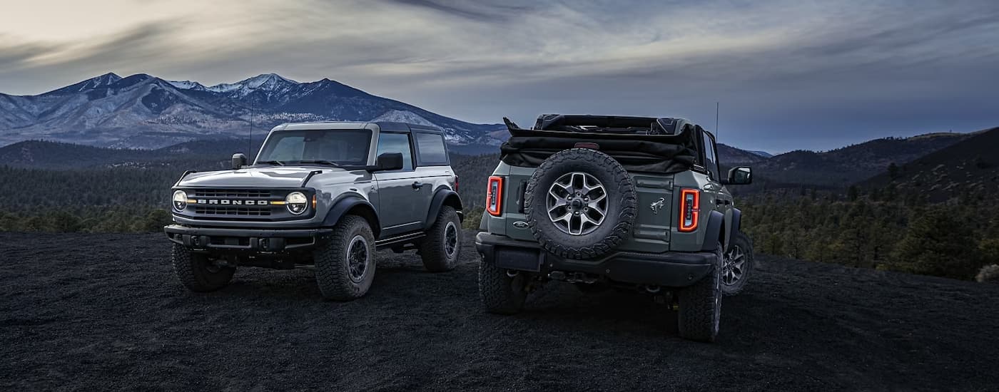 A grey 2024 Ford Bronco Black Diamond and grey a 2024 Ford Bronco Badlands parked off-road near mountains. class=