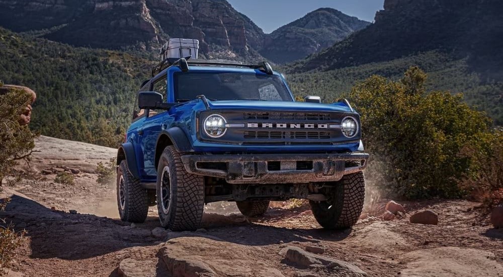 Ford Dealer Near Me - 2023 Ford Bronco - Mountains.jpg A blue 2023 Ford Bronco off-roading through the mountains with gear on the roof racks.