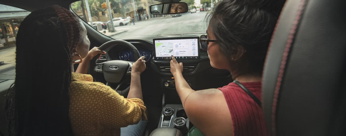 Two friends are shown driving in a 2024 Ford Escape for sale on a city street.