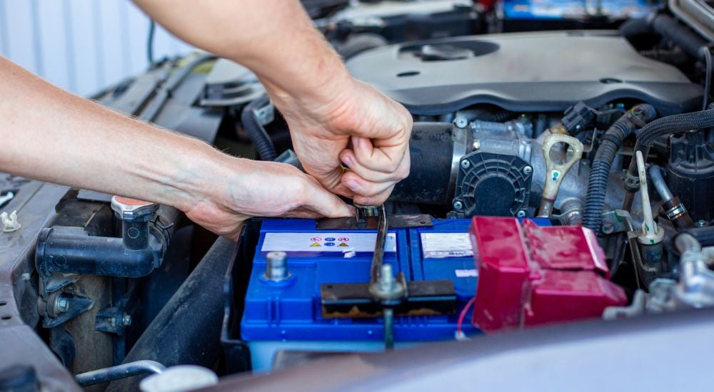 A close up shows a mechanic tightening a battery strap.