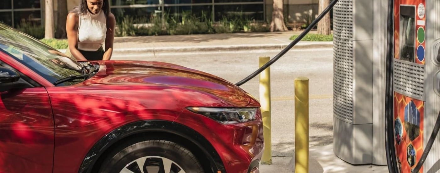 A woman plugging in a red 2024 Ford Mustang Mach-E into a charging station.