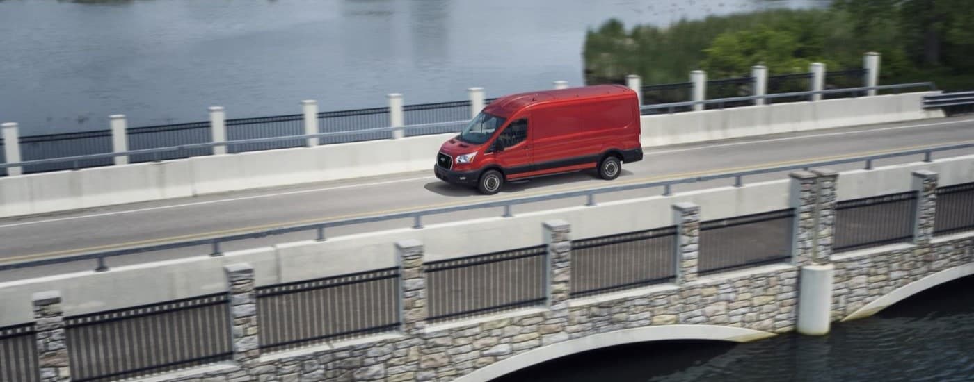 A red 2023 Ford Transit driving over a bridge.