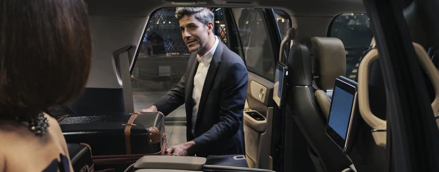 A well-dressed man stowing luggage in a black 2023 Lincoln Navigator.