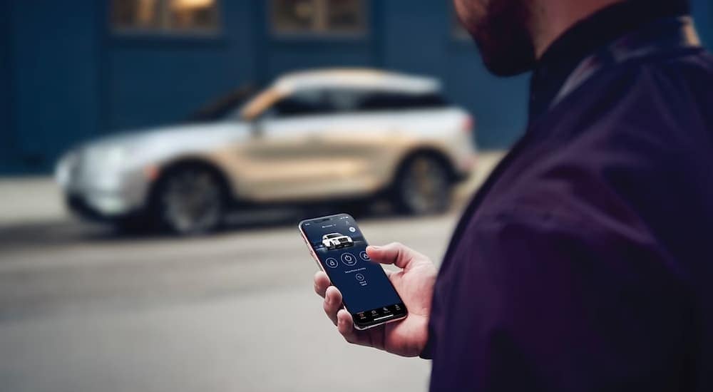 A man using his smartphone app to remote start a silver 2024 Lincoln Corsair.