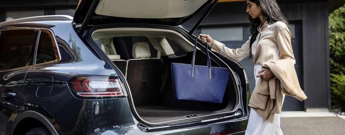 A woman placing a bag in the trunk of a blue 2023 Lincoln Nautilus.