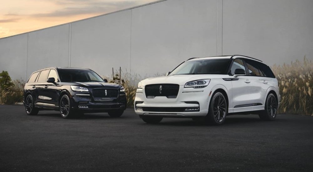 A black and a white 2023 Lincoln Aviator Black Label parked facing each other at a Lincoln dealer.