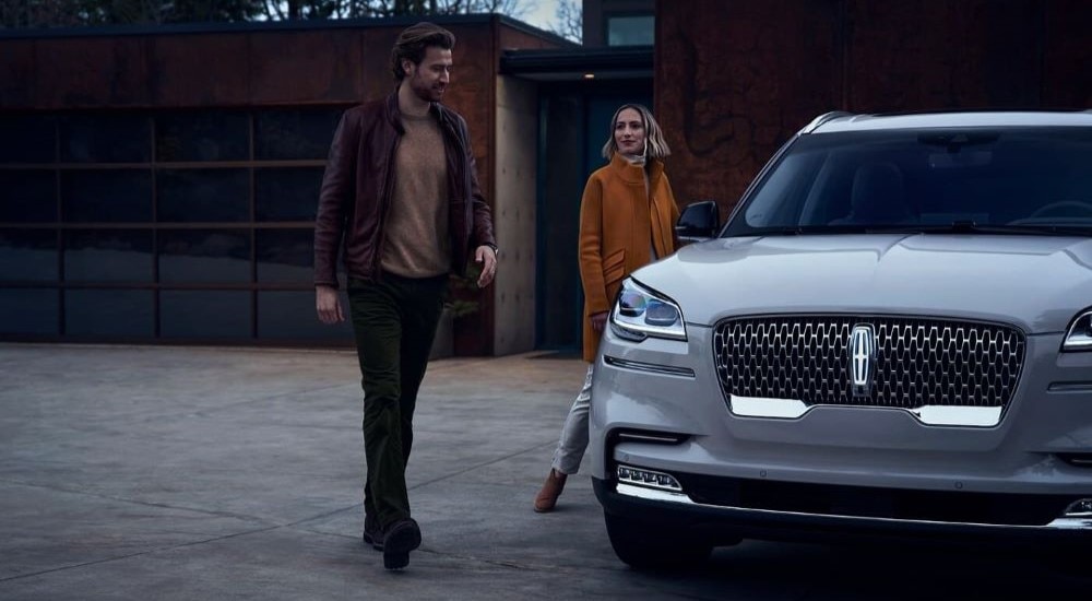A couple walking towards the silver 2023 Lincoln Aviator parked outside their modern home.