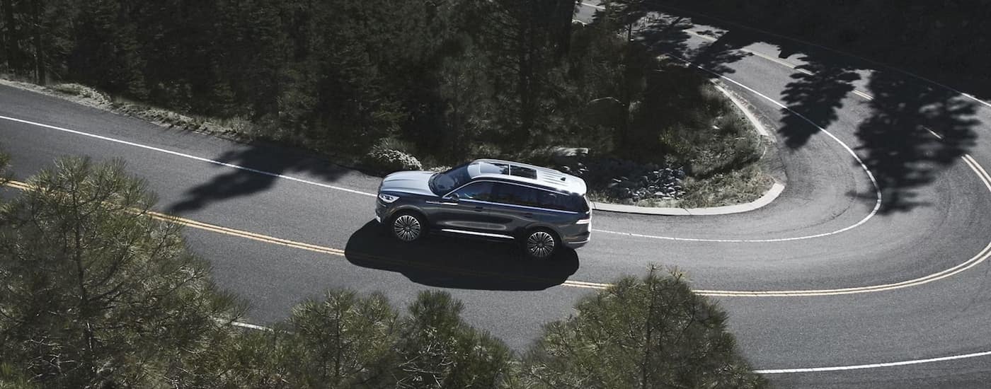 Aerial view of a silver 2023 Lincoln Aviator driving on a winding road lined with trees.