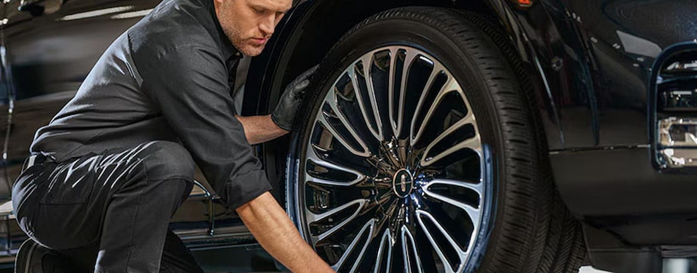 A close up of a mechanic replacing a tire on a black Lincoln SUV is shown.