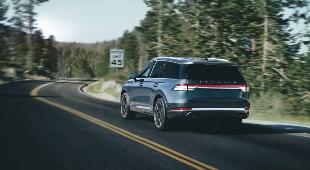 A blue 2023 Lincoln Aviator driving on a tree-lined road.